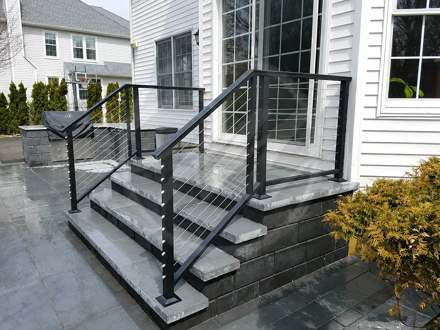Black cable railing around a gray stone residential entry stair and landing