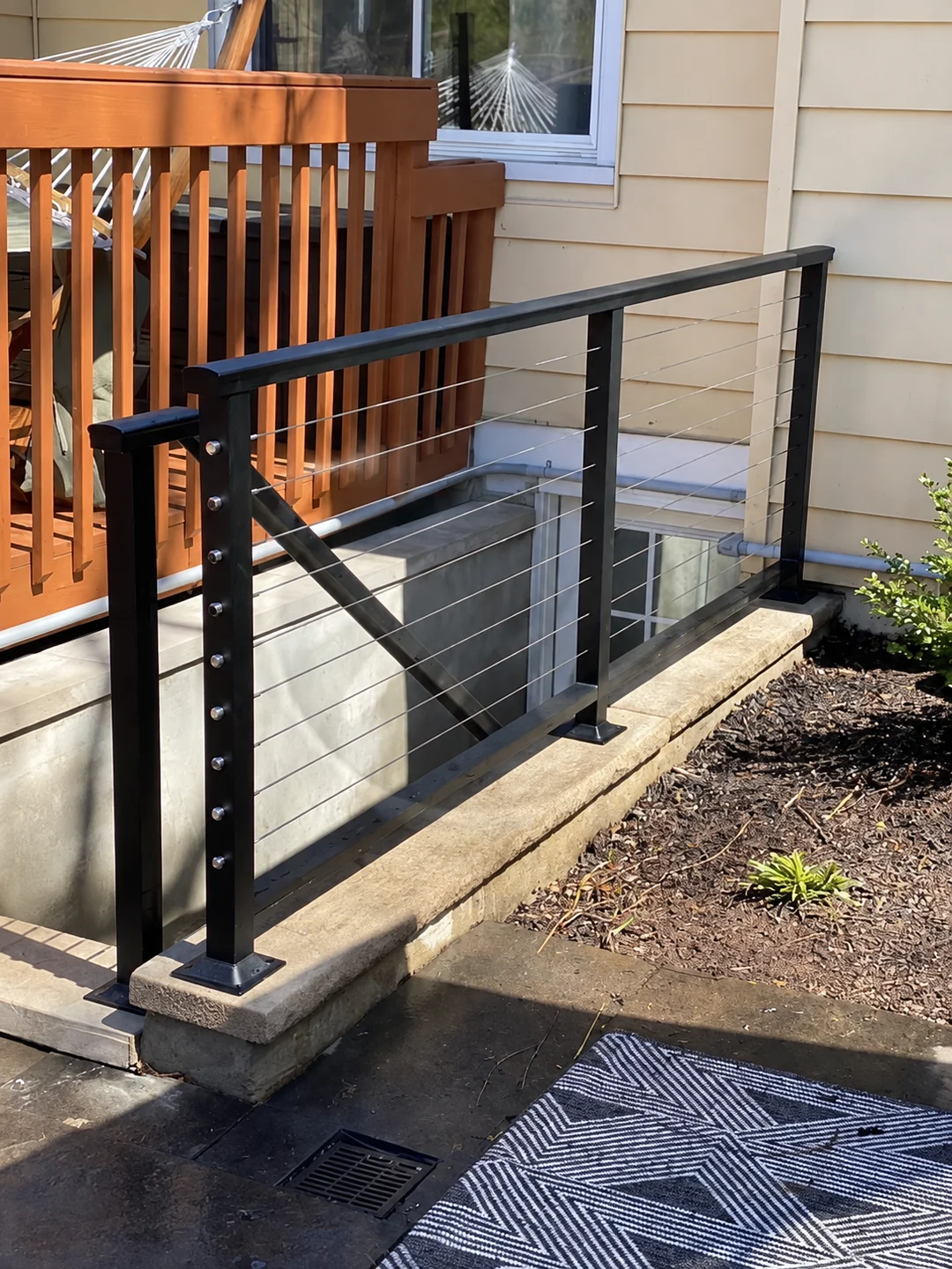 Black cable railing on a residential exterior stair beside a wood deck