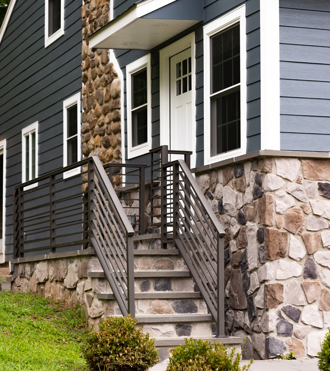 Dark horizontal-picket railing on the front steps of a stone-and-siding home