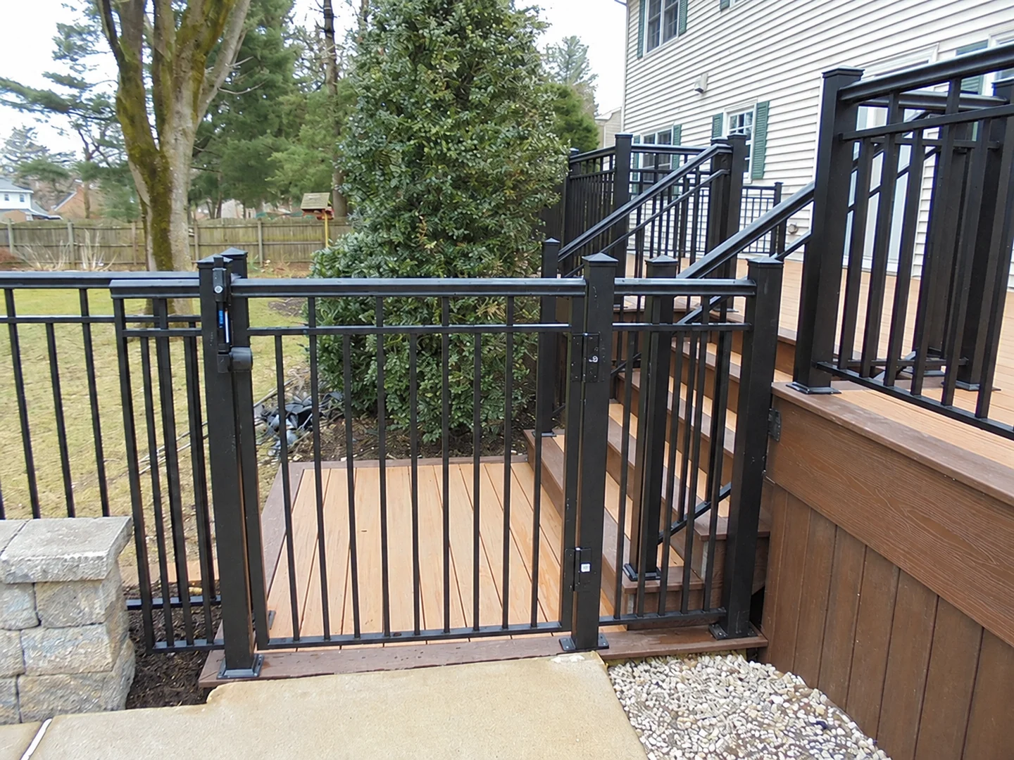 Black metal gate integrated with dark deck railing and wood deck stairs
