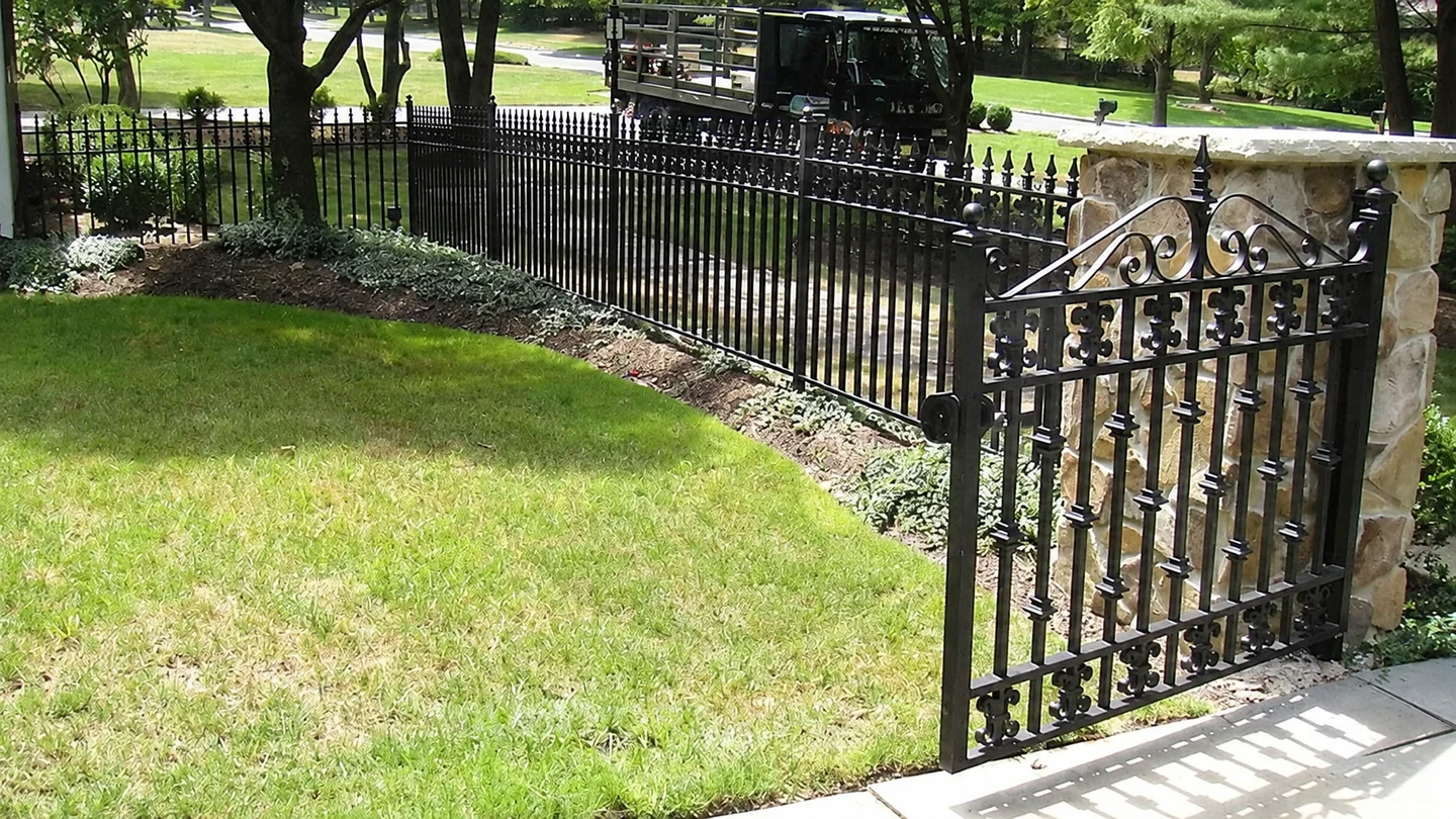 Decorative black metal gate connecting to a matching ornamental fence line beside a landscaped lawn