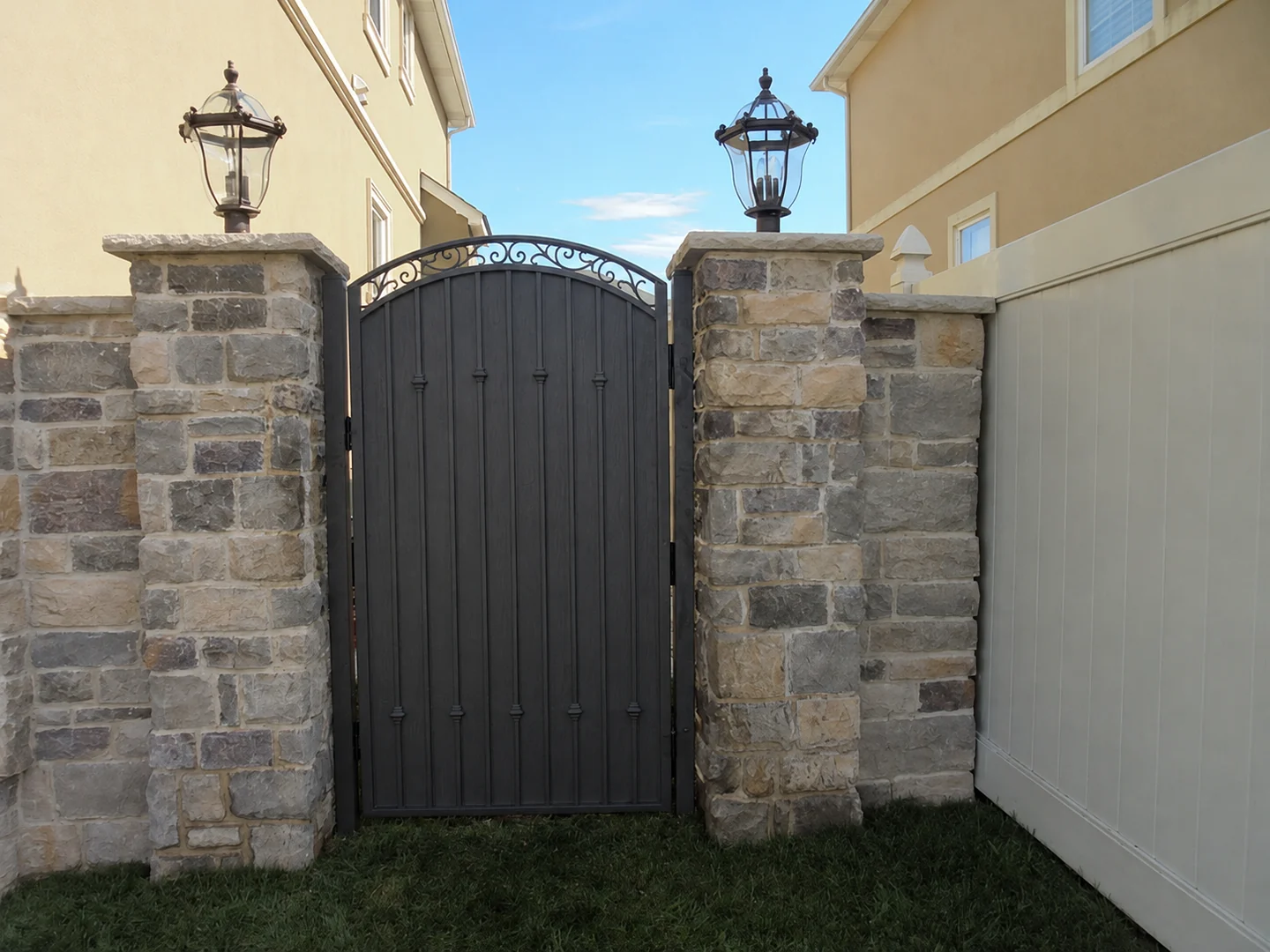 Black privacy gate between stone entry pillars beside a white privacy fence