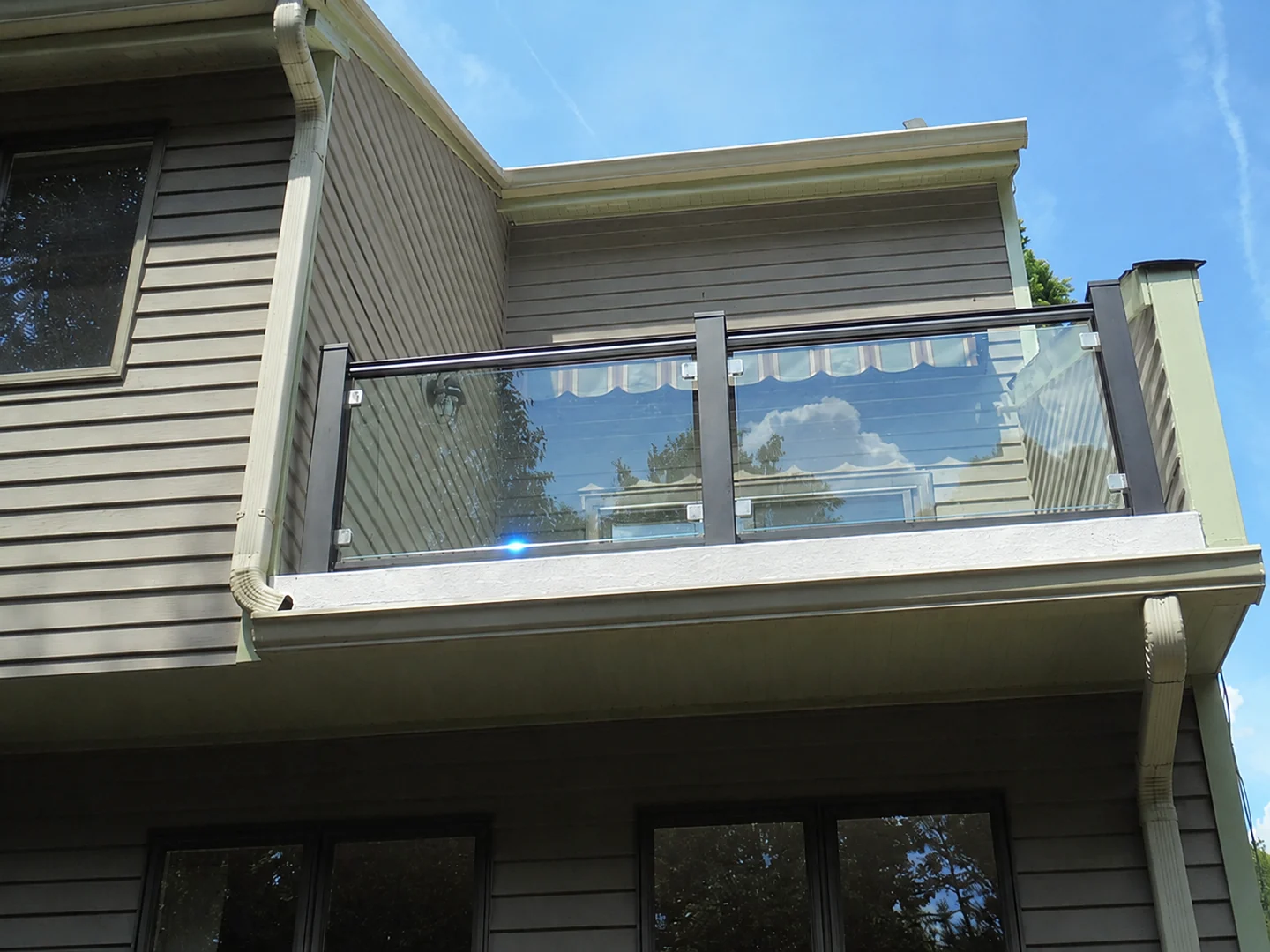 Transparent glass balcony railing with dark posts and clamps on a residential exterior