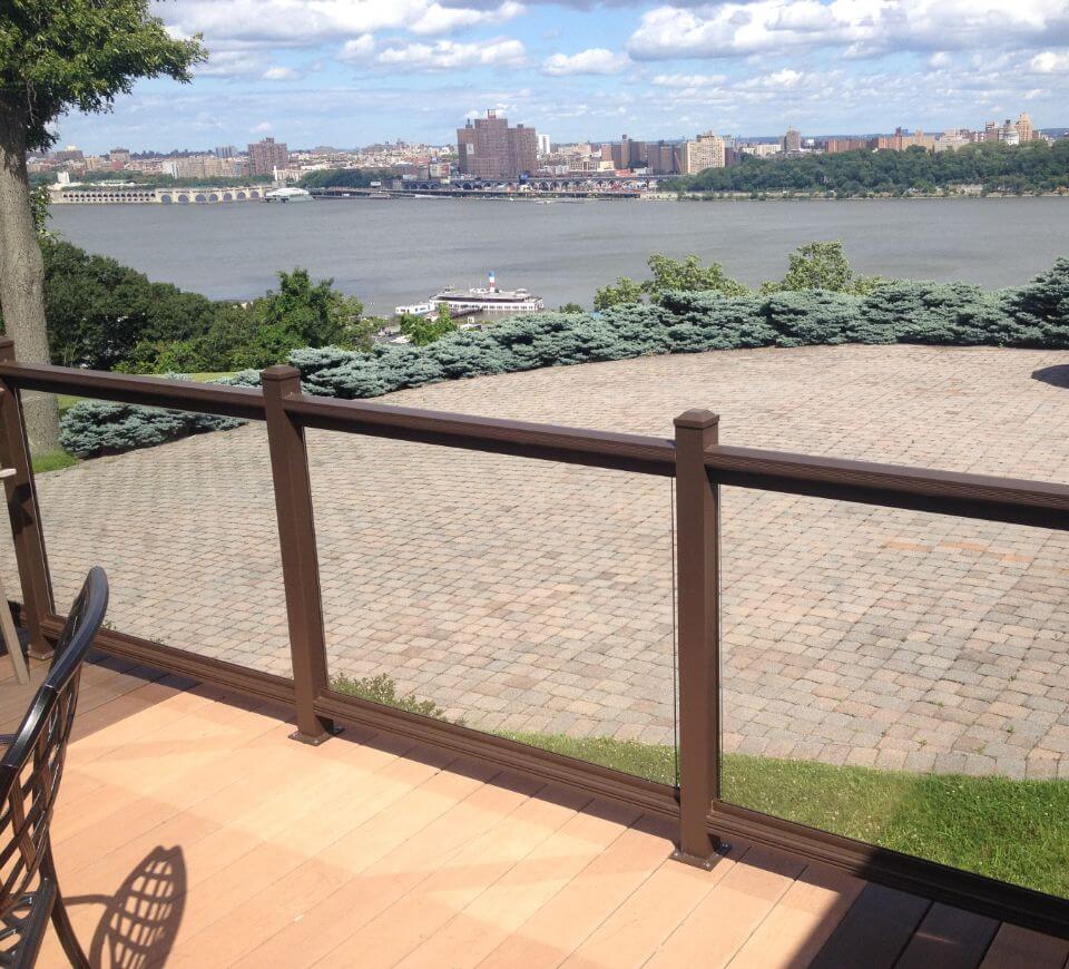 Brown-framed glass railing installed along a residential patio overlooking the river