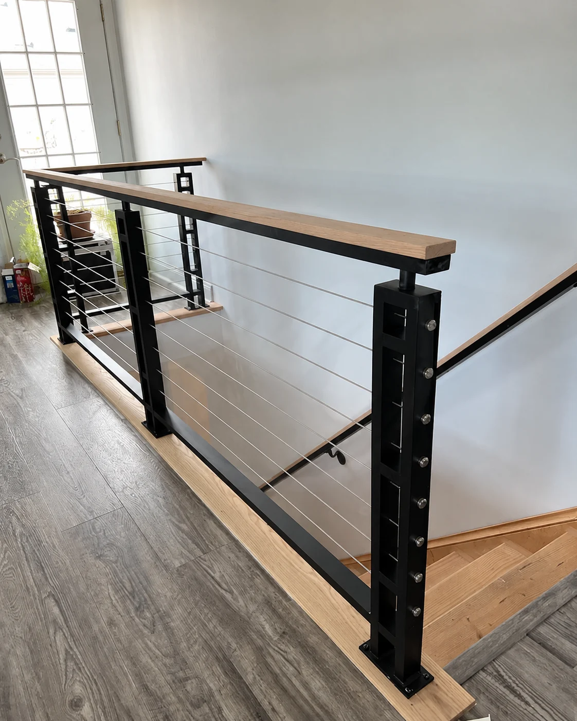 Black cable railing with a light wood handrail at a finished interior landing