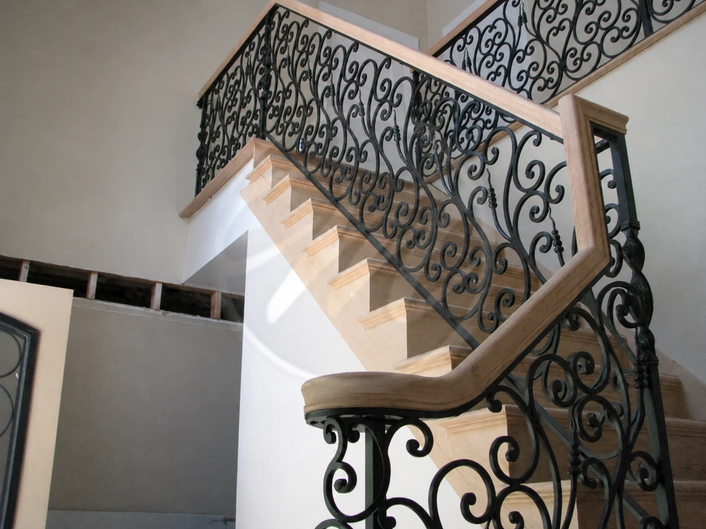 Custom black scrollwork stair railing paired with a light wood handrail inside a home