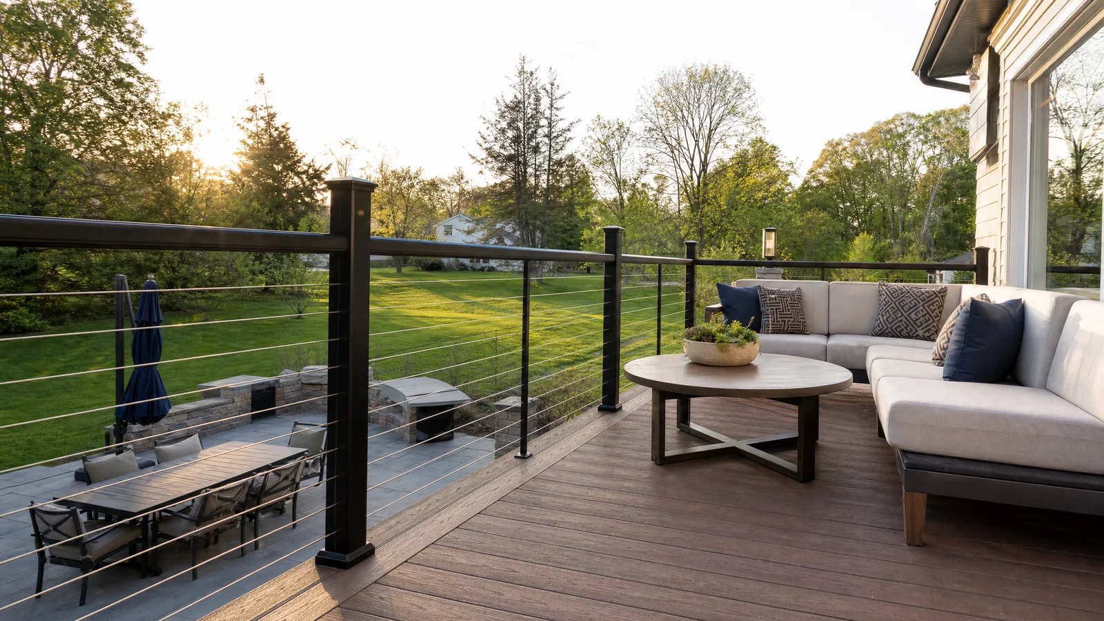 Black cable railing surrounding a furnished residential deck overlooking a backyard